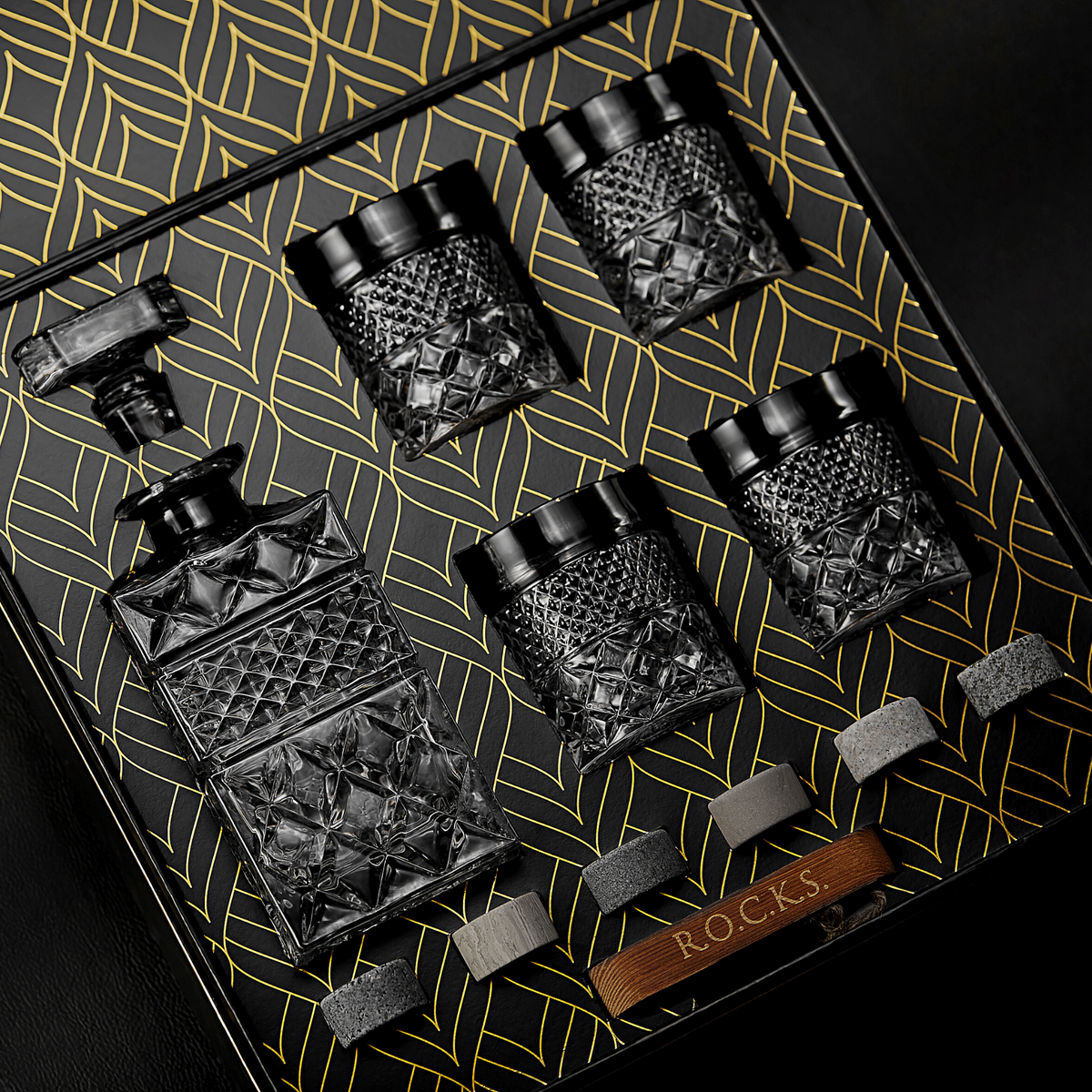 Close view of a crystal whiskey decanter, whiskey glasses and granite chilling stones in presentation packaging